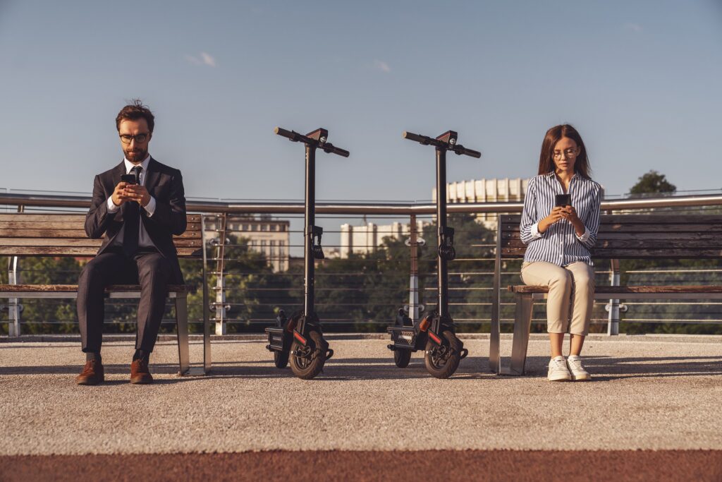 Chicago e-Scooter Do's and Don'ts image. Young business man and business woman sitting on a bench and using their phones while riding electric scooters on the background of the morning city.