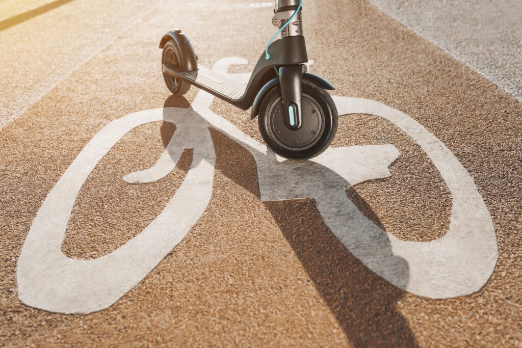 Street Legal or Not? Using Micromobility on the Road image. Close up of electric scooter or kick scooter at cityscape on bicycle road sign way